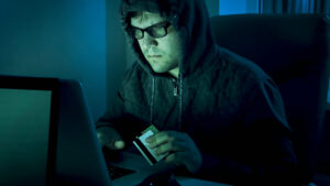 Man in glasses and hoodie holding credit card while looking at laptop